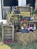 Houten kratten, uitgestald op stro, tonen knoflook, aardappelen, flessen en kleine potjes op een groentemarkt in de openlucht.