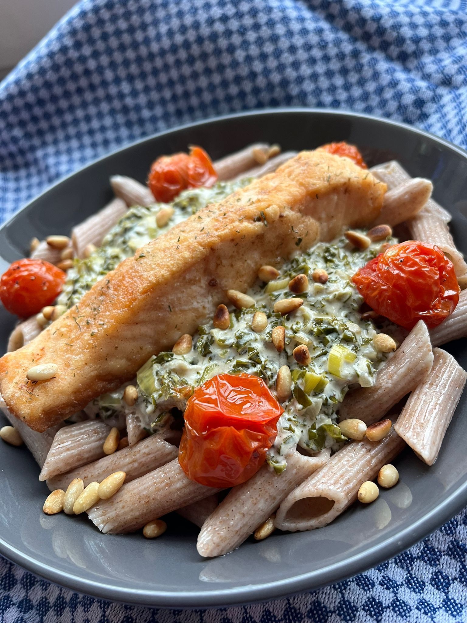 Een gebakken zalmfilet geserveerd op volkoren penne pasta, gegarneerd met een romige spinaziesaus, tomaten en pijnboompitten.