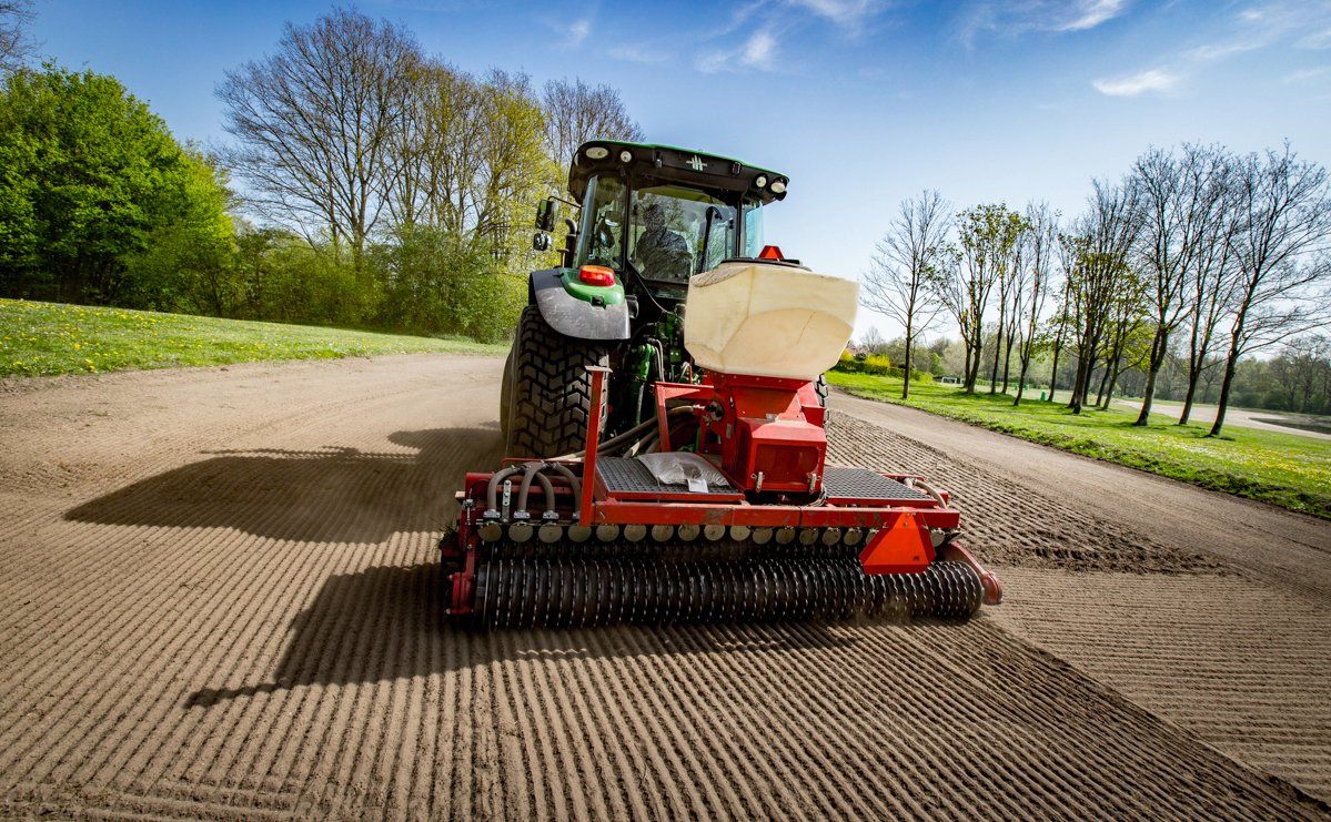 Op een zonnige dag trekt een tractor een zaaimachine over een pas geploegd veld.