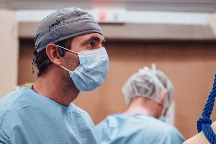 Un chirurgien portant un masque et une casquette se tient debout dans une salle d'opération.