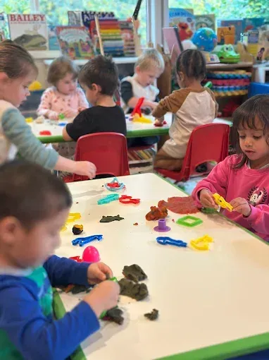 Children at tables, playing with colorful playdough and tools in a classroom.