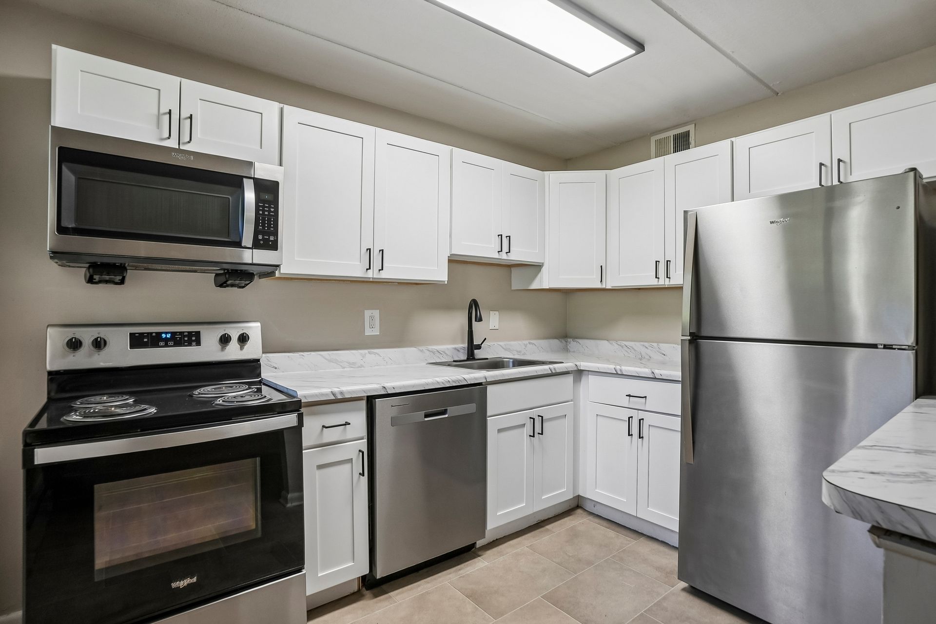 Modern white kitchen with stainless steel appliances, and black fixtures.