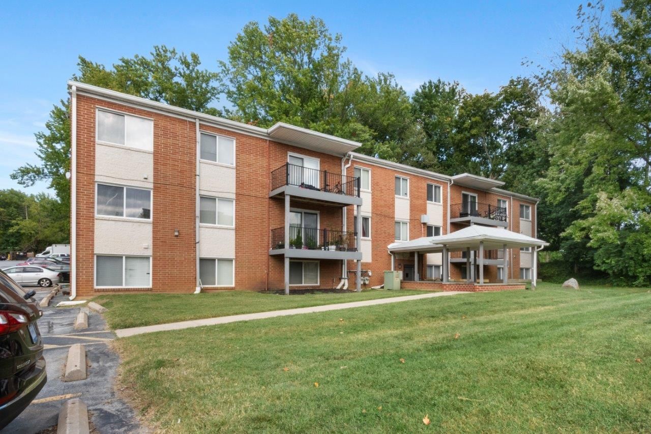 Exterior view of a brick apartment building with balconies, green lawn, and parked cars at Westover Pointe in Wilmington, DE.