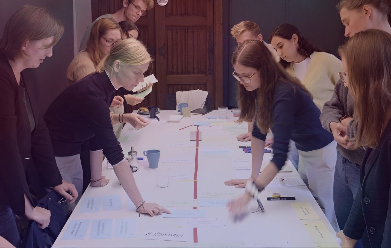 Eine Gruppe von Menschen arbeitet an einem Tisch mit Materialien und Notizen; Bildquelle: Projektitekt