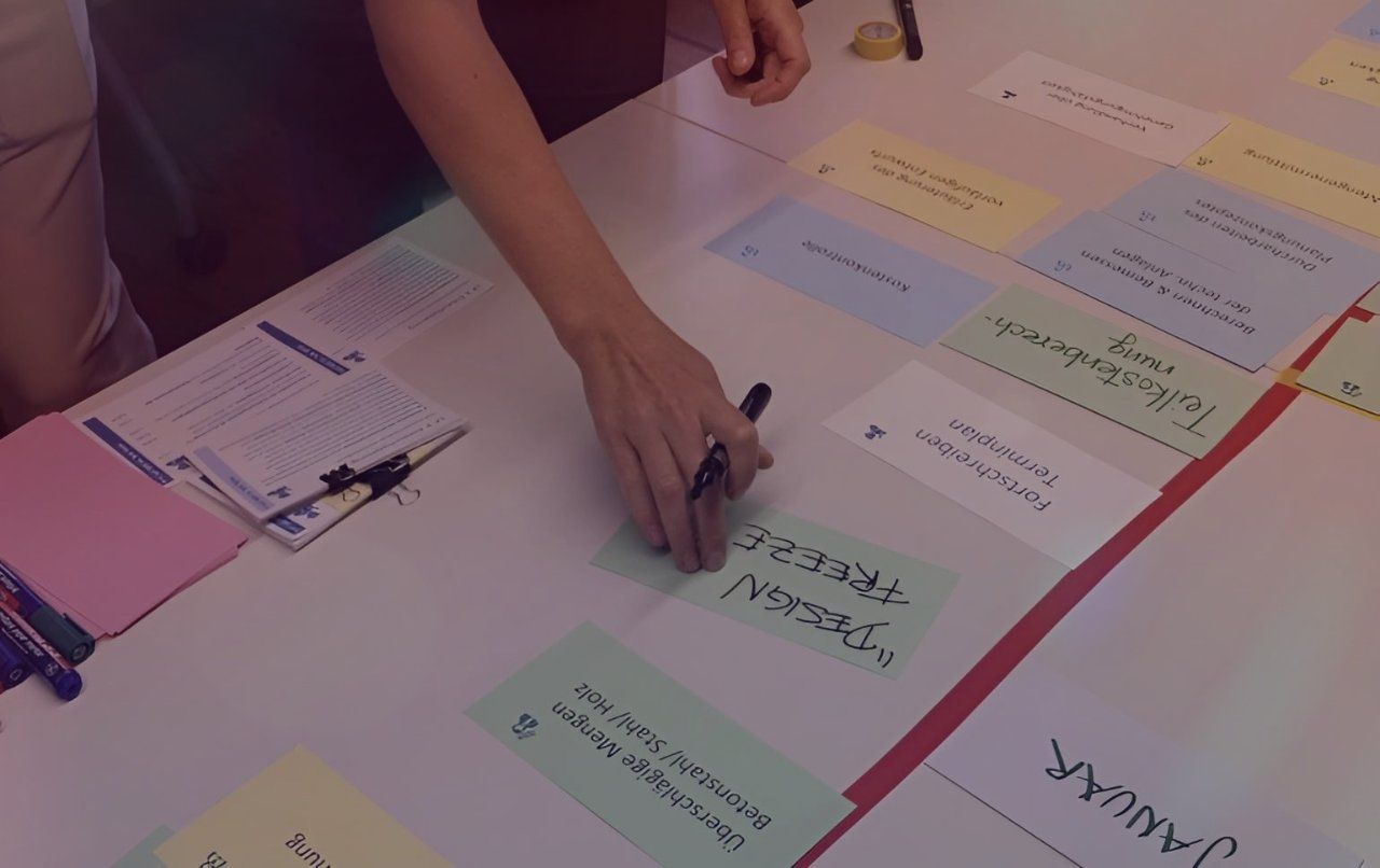 Eine Hand schreibt auf ein Flipchart mit bunten Karten und Notizen auf einem Tisch; Bildquelle: Projektitekt