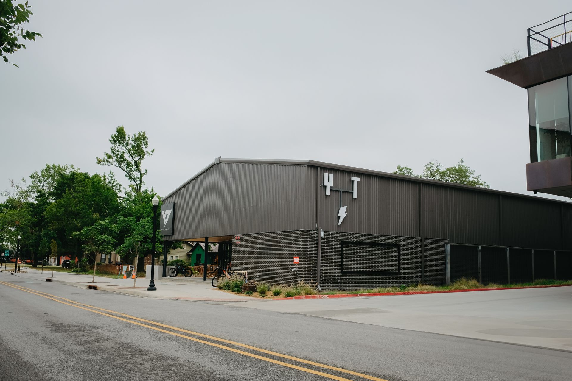 Dark grey industrial building on a street corner with a mural and a modern building on the right.