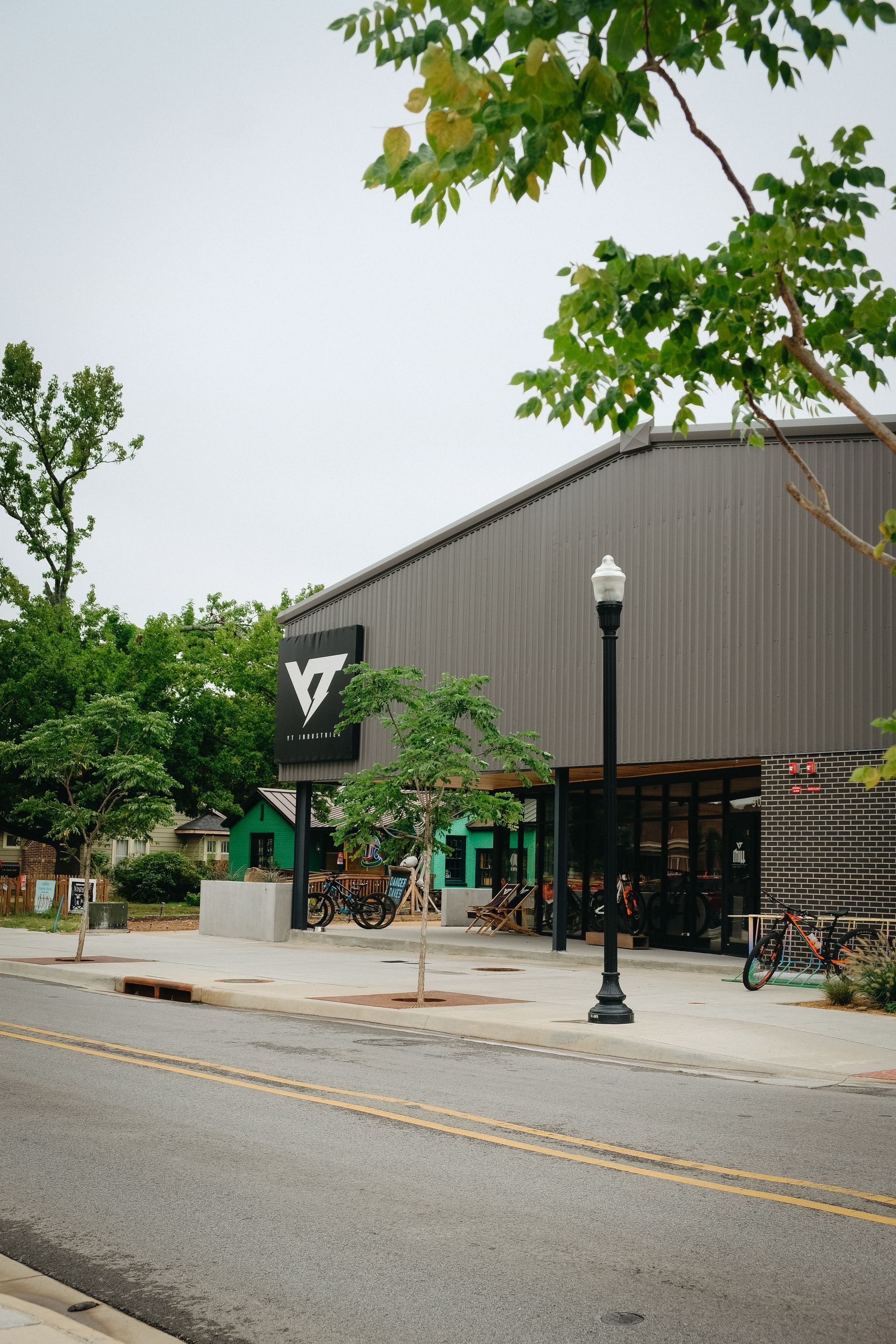 Gray building with black sign, street, sidewalk, trees.