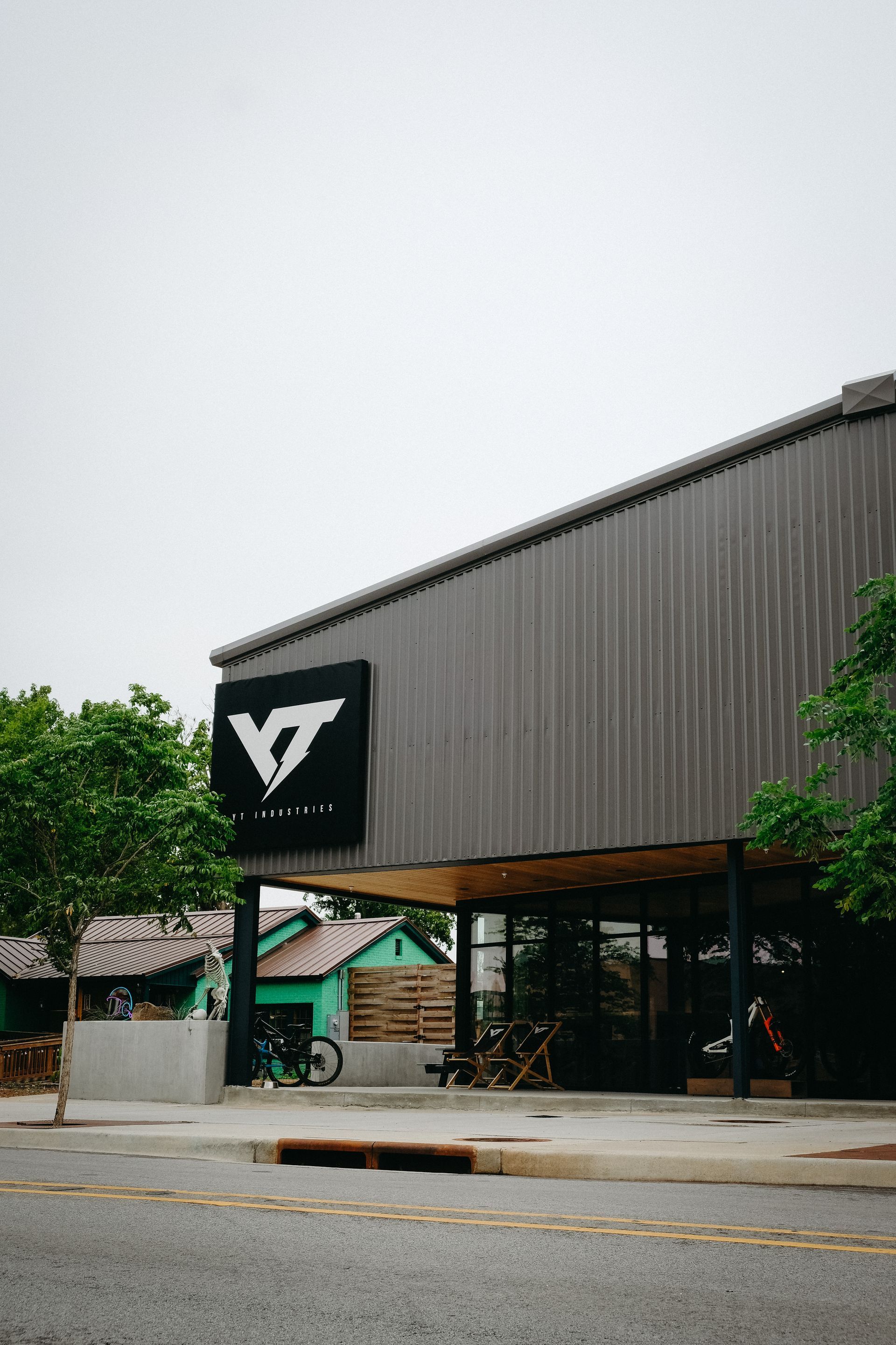 Bike shop with large black logo, metal siding, glass front, bikes on display. Cloudy day.