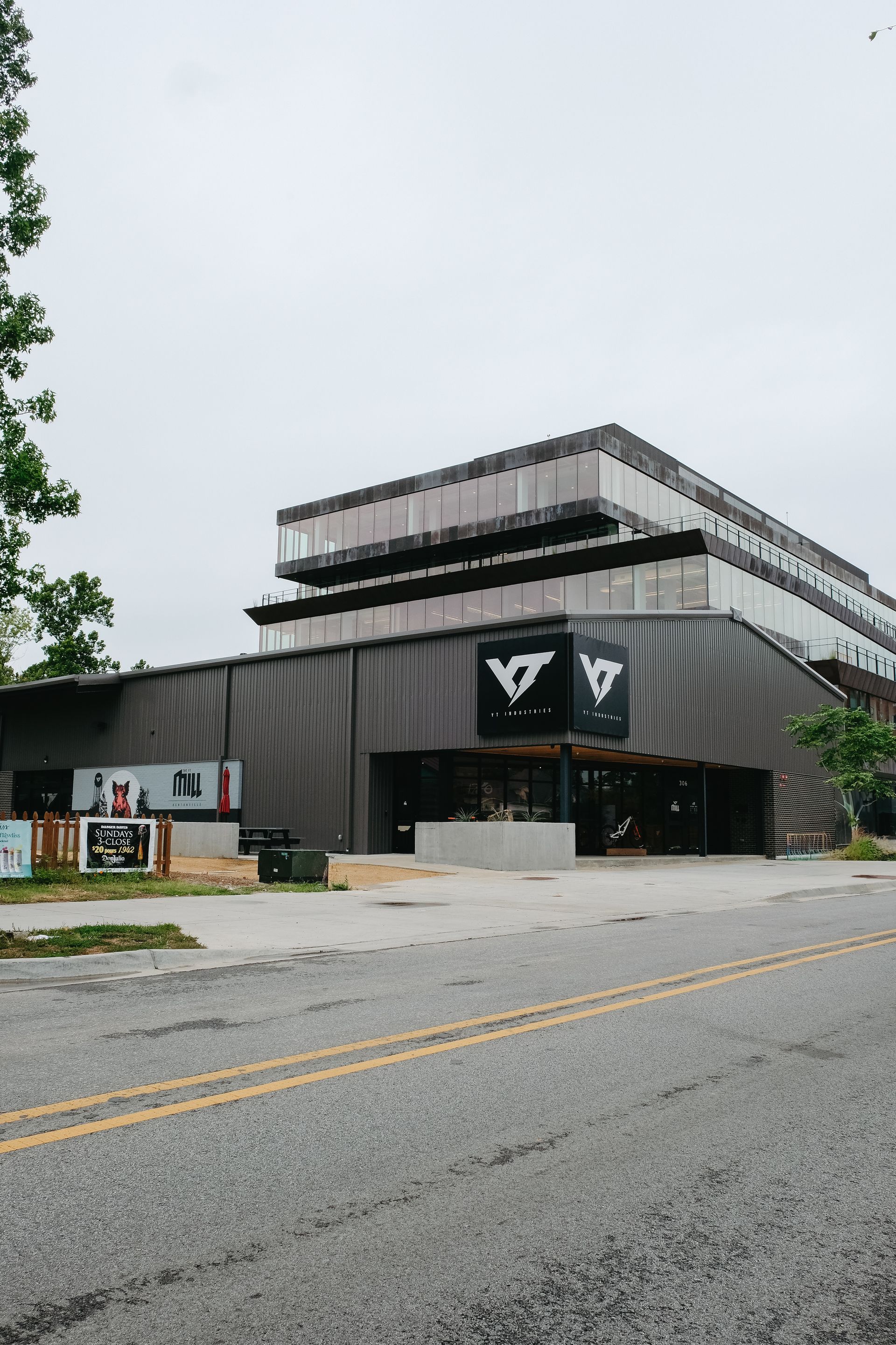 Gray building with black sign, next to a multi-story building on a cloudy day.