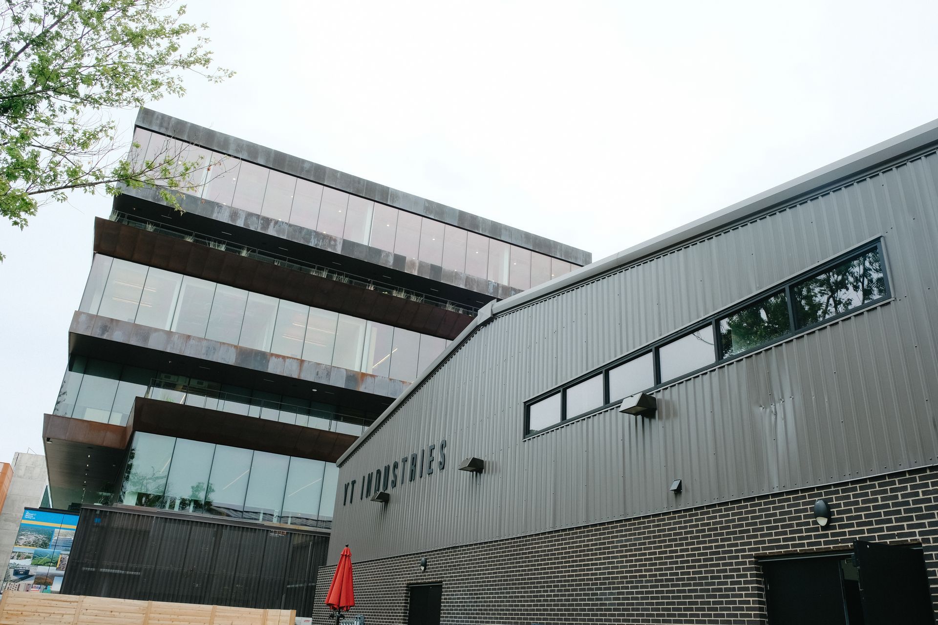 Modern building exterior, with glass and metal. One section brick. Cloudy sky.