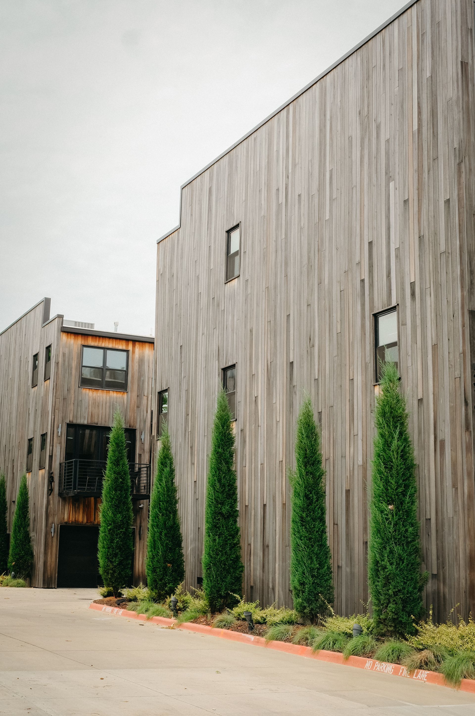 Wooden buildings with vertical siding, green trees, and a gray sky.