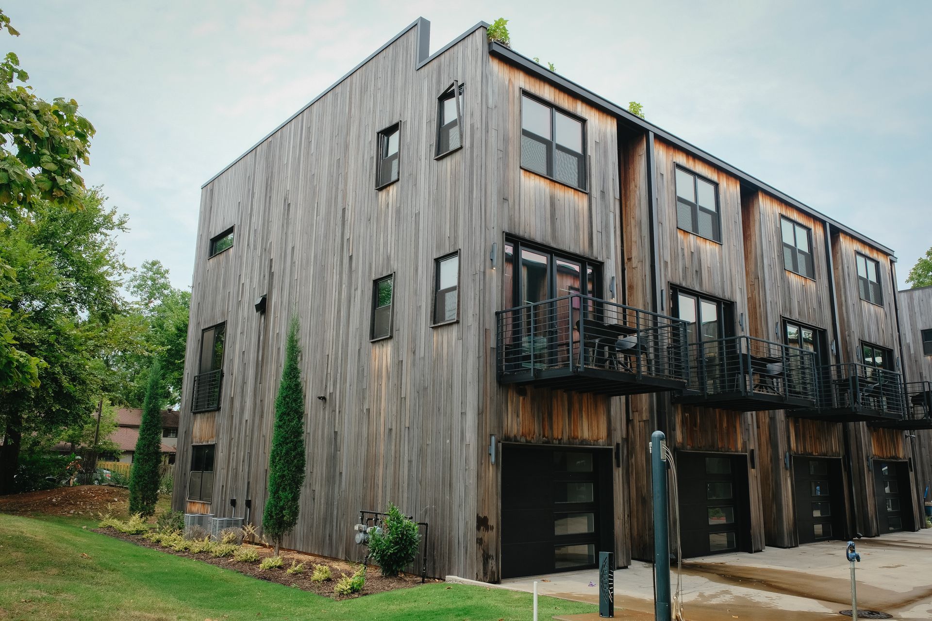 Modern townhouses with weathered wood siding, balconies, and garage doors.