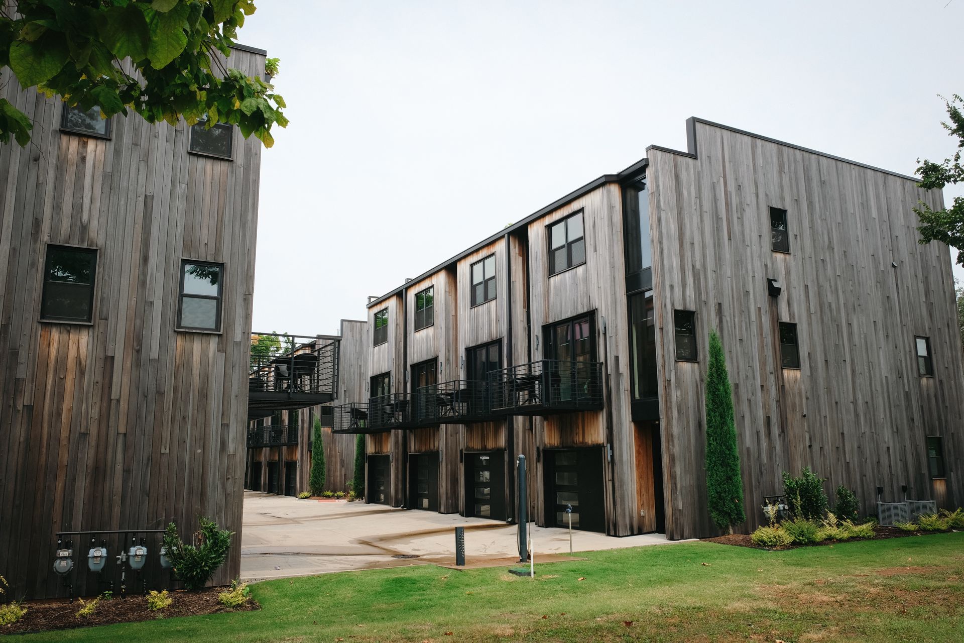 Townhouses with weathered wood siding and small balconies. Grass in foreground; cloudy sky above.
