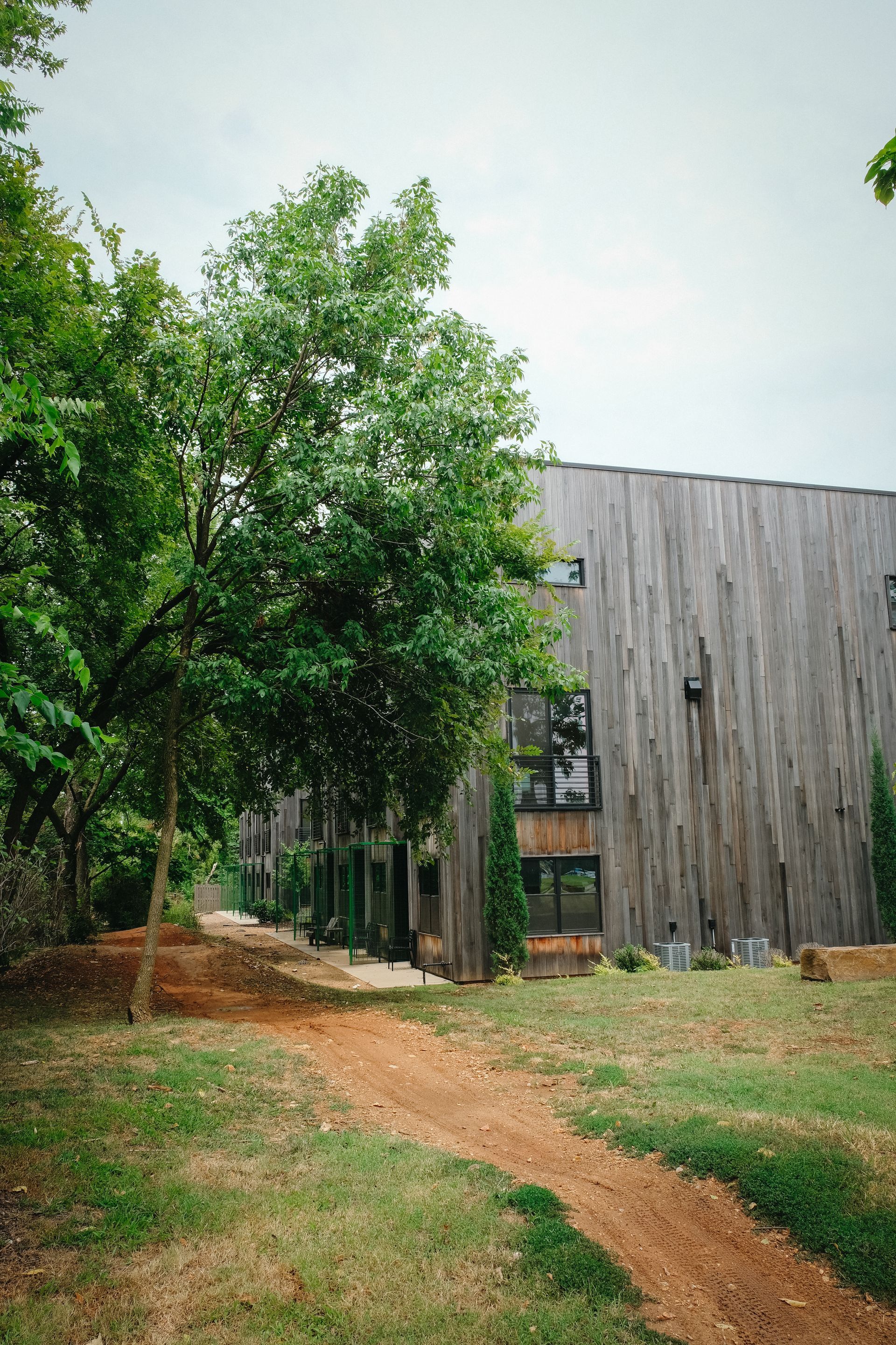 Wooden building nestled in a wooded area with a dirt path leading to the entrance.