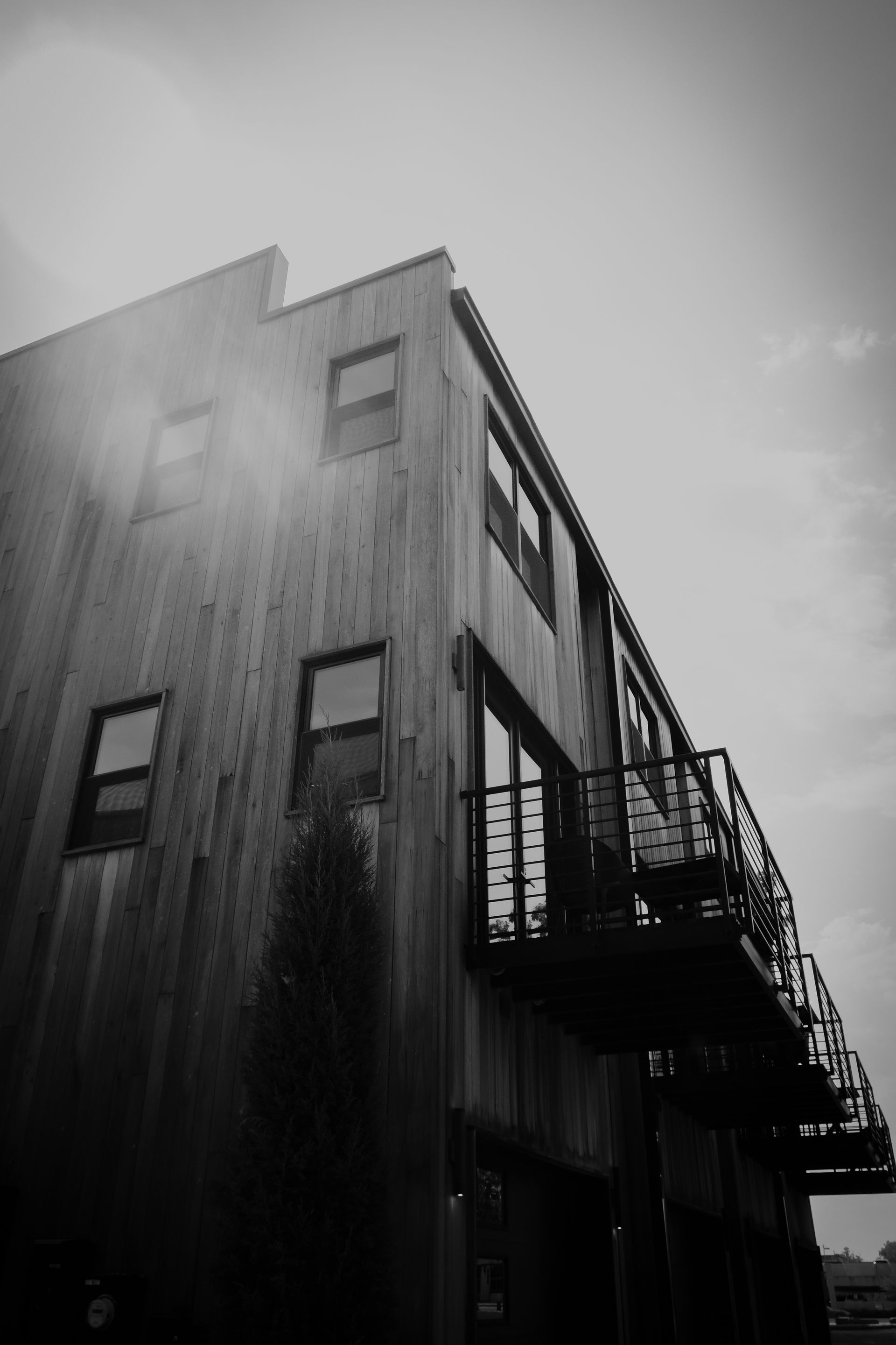 Black and white shot of a modern wooden building with a balcony against a bright sky.