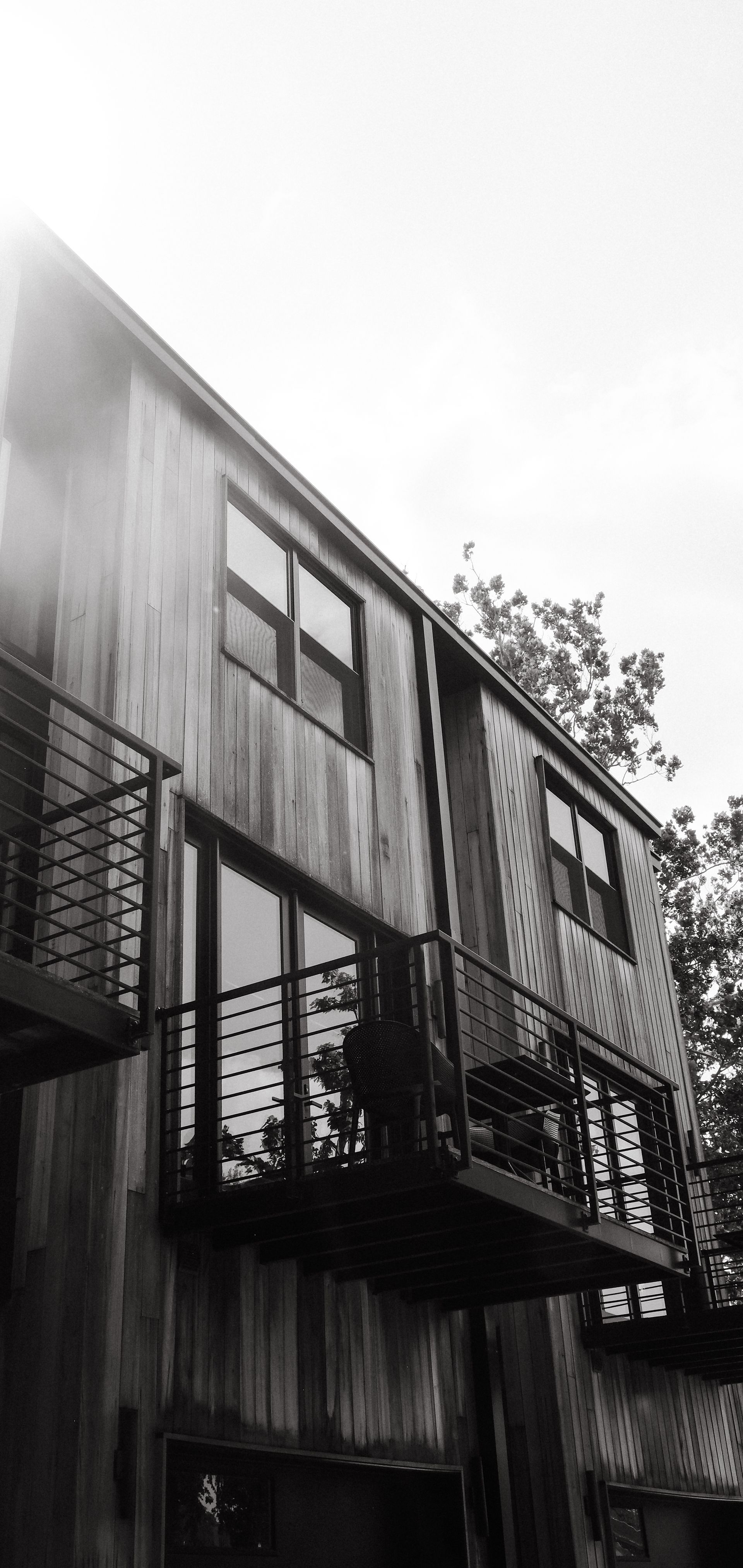 Black and white photo of a wooden two-story house with balconies and large windows.