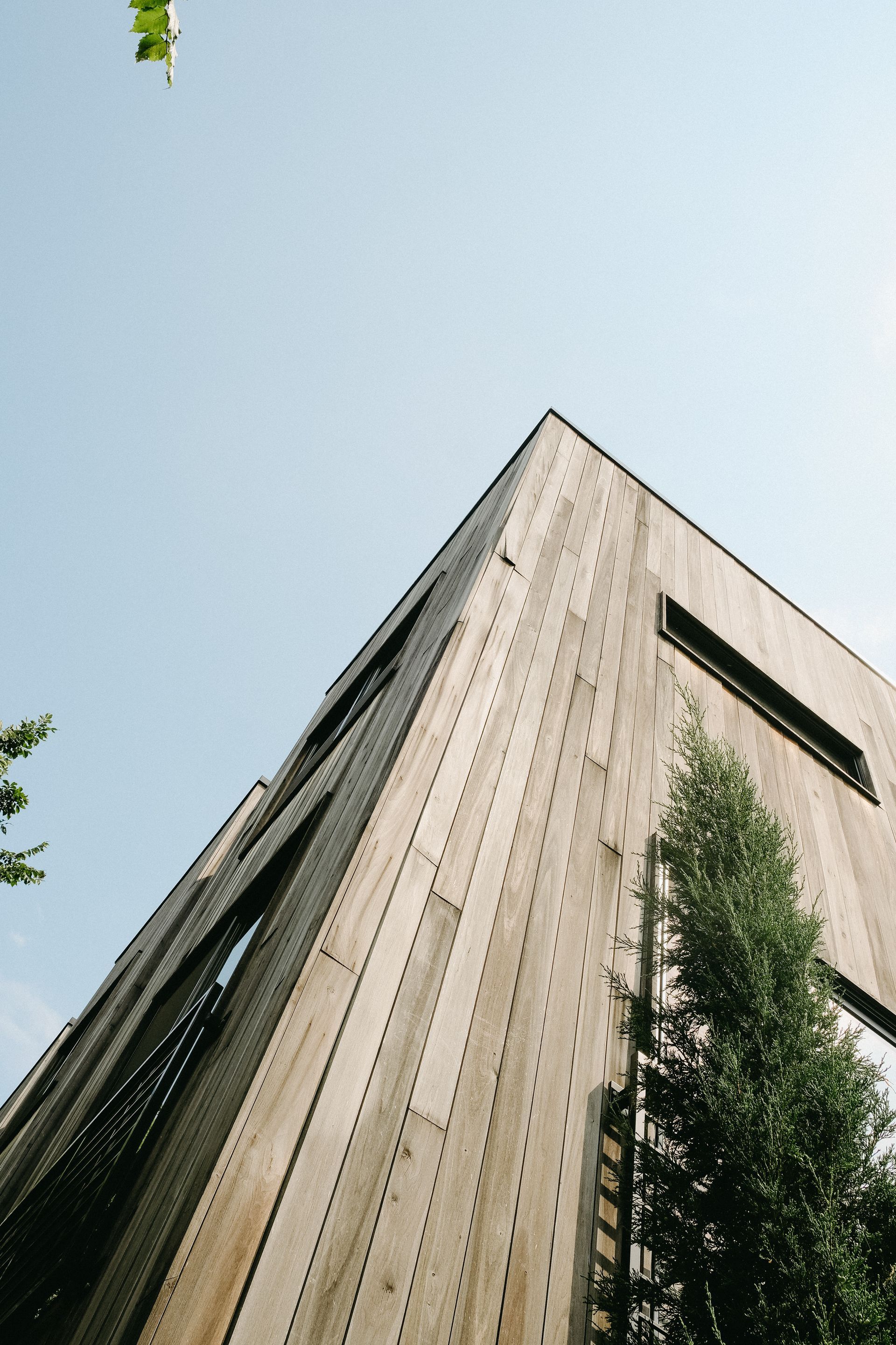 Wooden building with a sharp angle, reaching toward a clear blue sky.