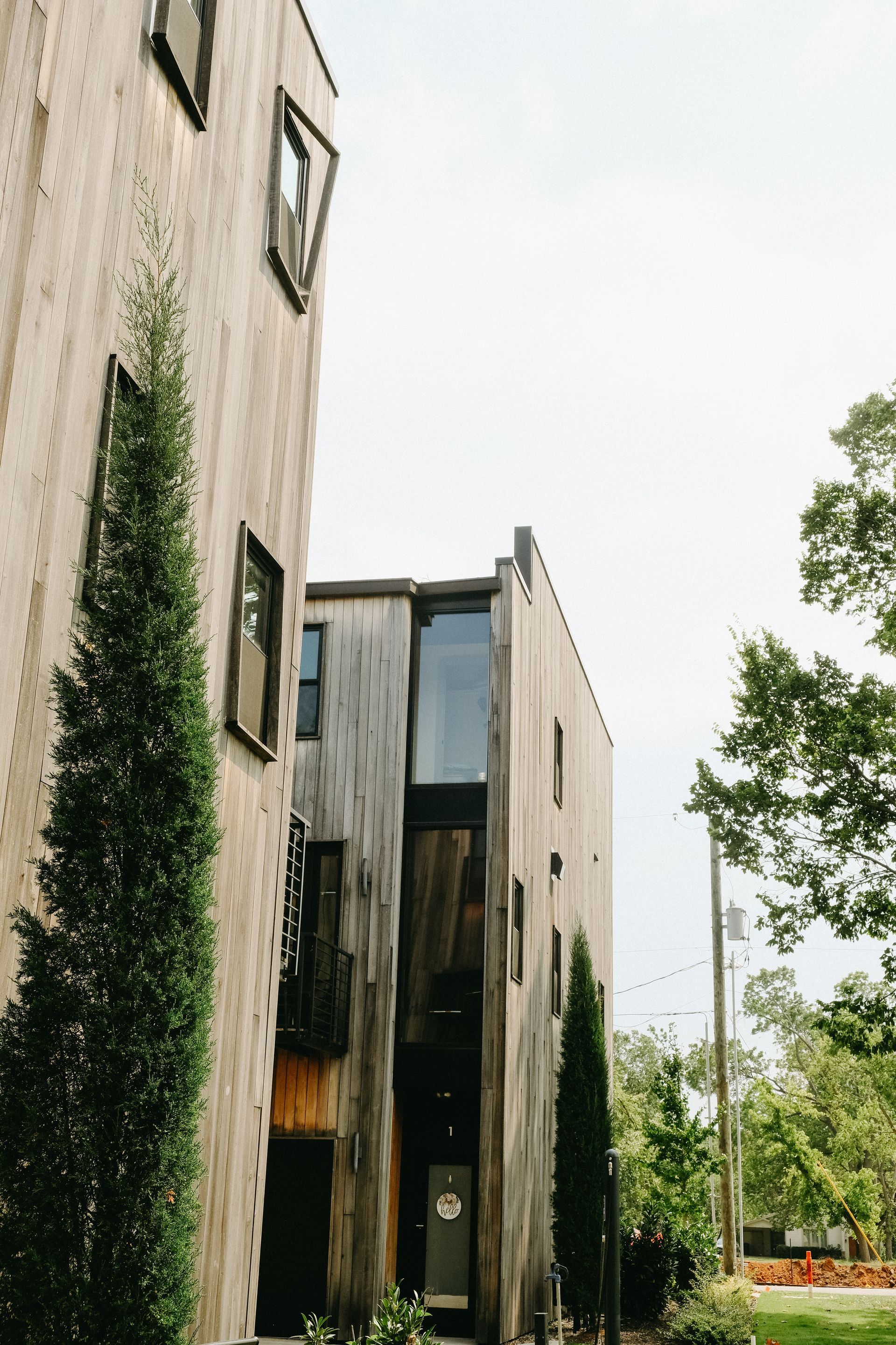 Three-story wood buildings, tall and narrow, with windows. Green trees, cloudy sky.