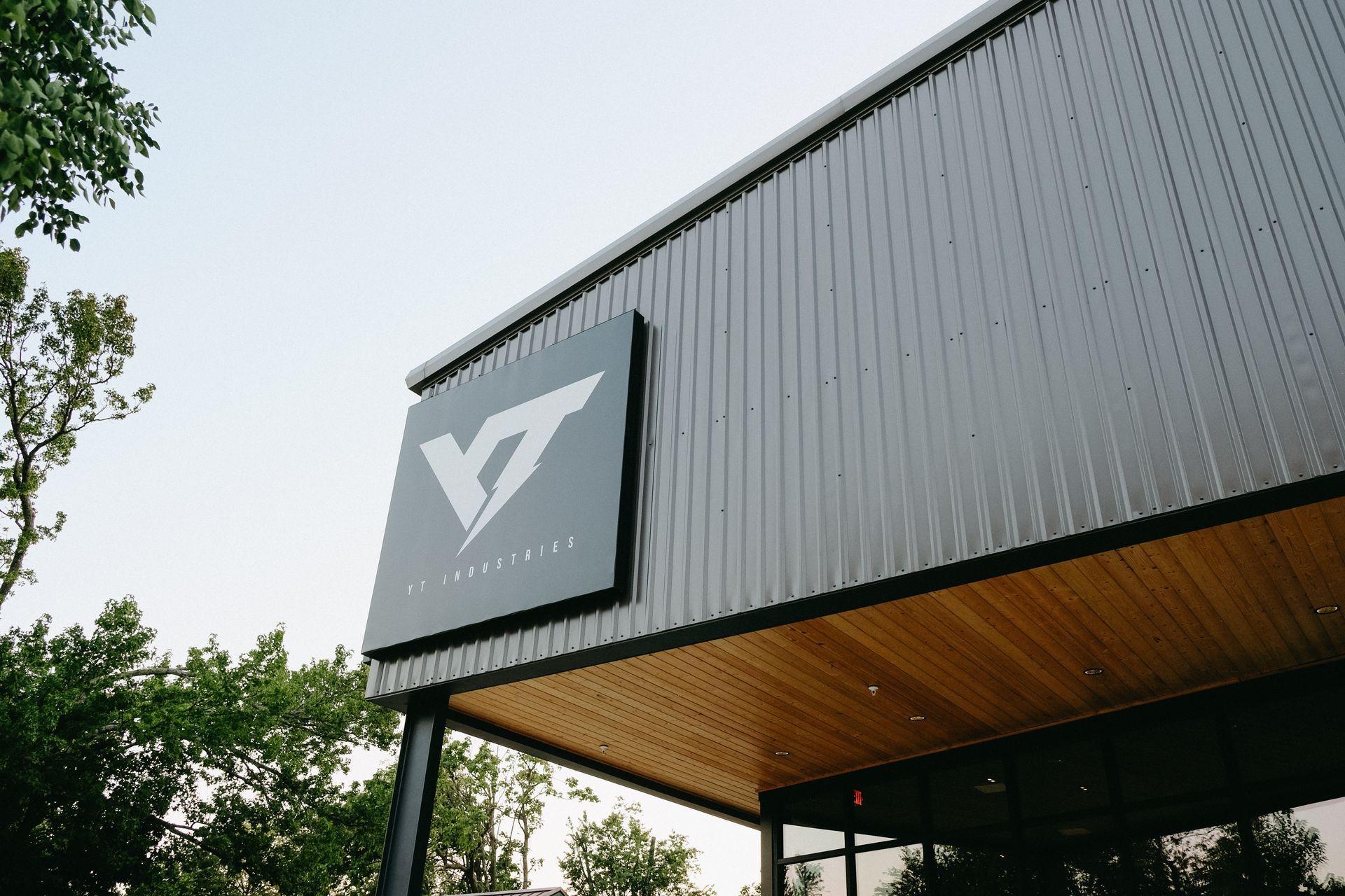Sign for Vitesse Club on a building exterior, dark gray metal siding, light wood under the eaves, daytime.
