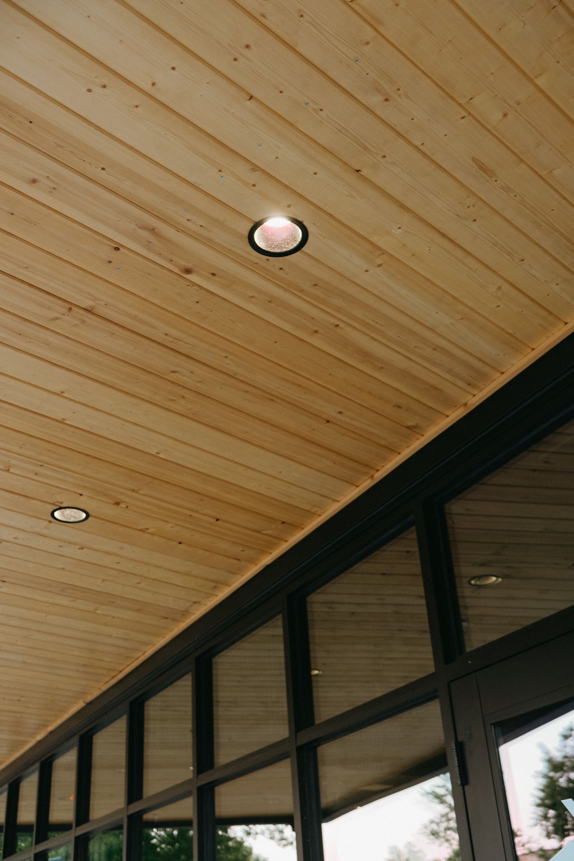 Wooden ceiling with recessed lights over large windows.