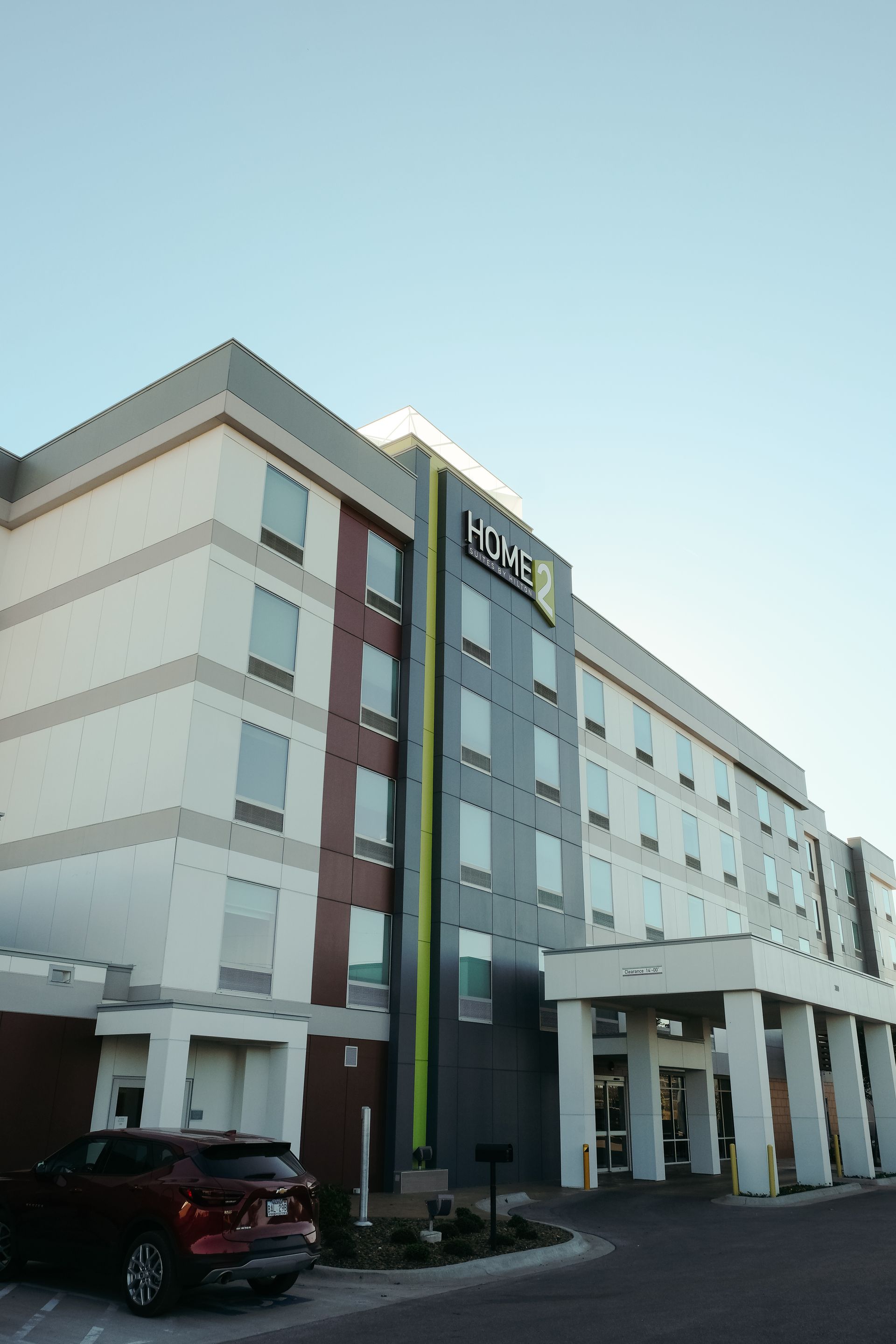 Modern hotel exterior with a white, gray, and red facade, and a car parked nearby.
