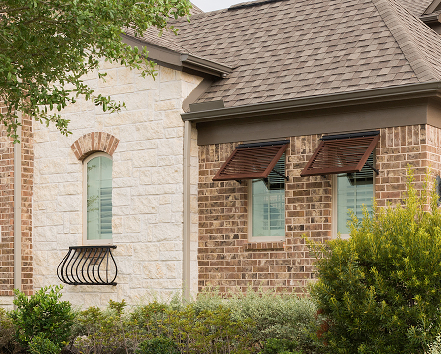 House exterior with brick and stone, brown roof, and two windows with open awnings.