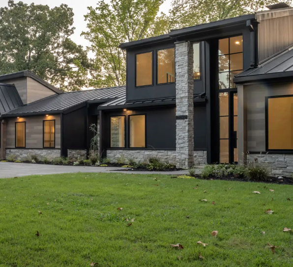 Modern home with black and stone facade, large windows, and green lawn.