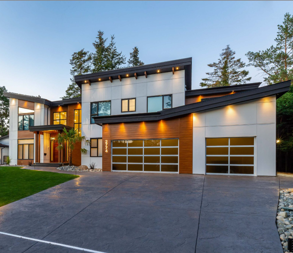 Modern house with gray concrete driveway, glass garage doors, and wood accents.