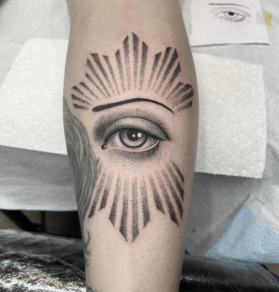 A black and white tattoo of an eye with rays coming out of it