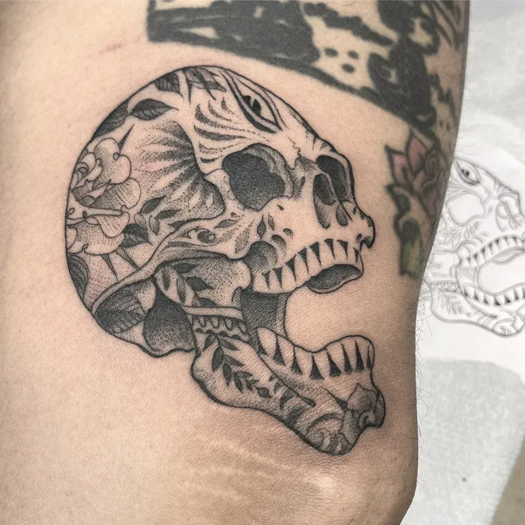 A black and white tattoo of a skull with flowers on it