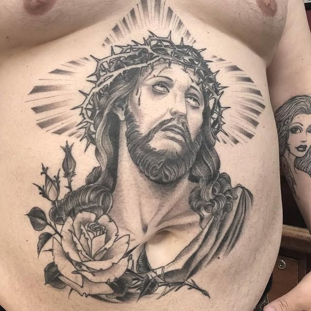 A man has a tattoo of jesus with a crown of thorns on his chest