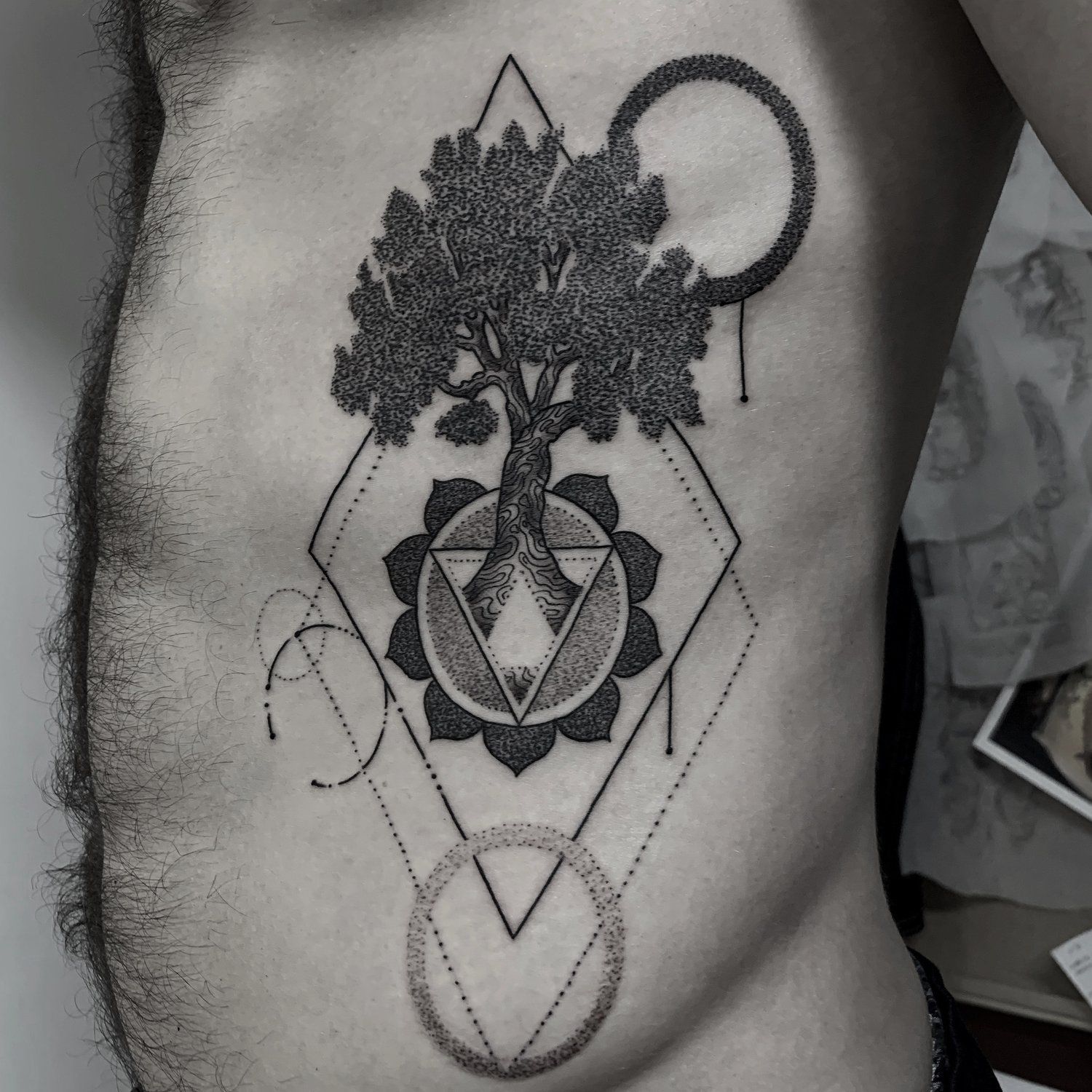 A man has a black and white tattoo of a tree and geometric shapes on his side.