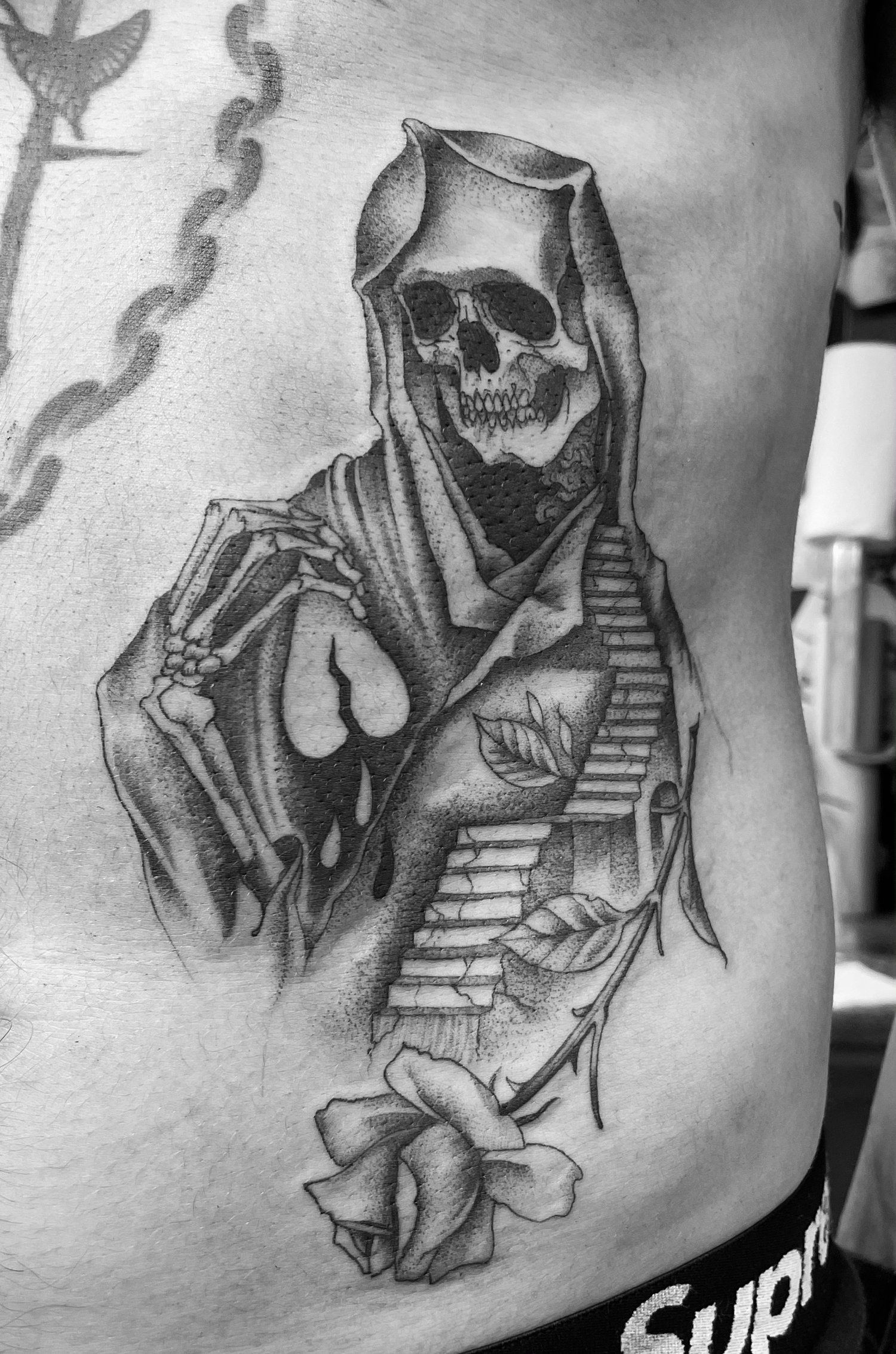 A black and white photo of a grim reaper tattoo on a person 's side.