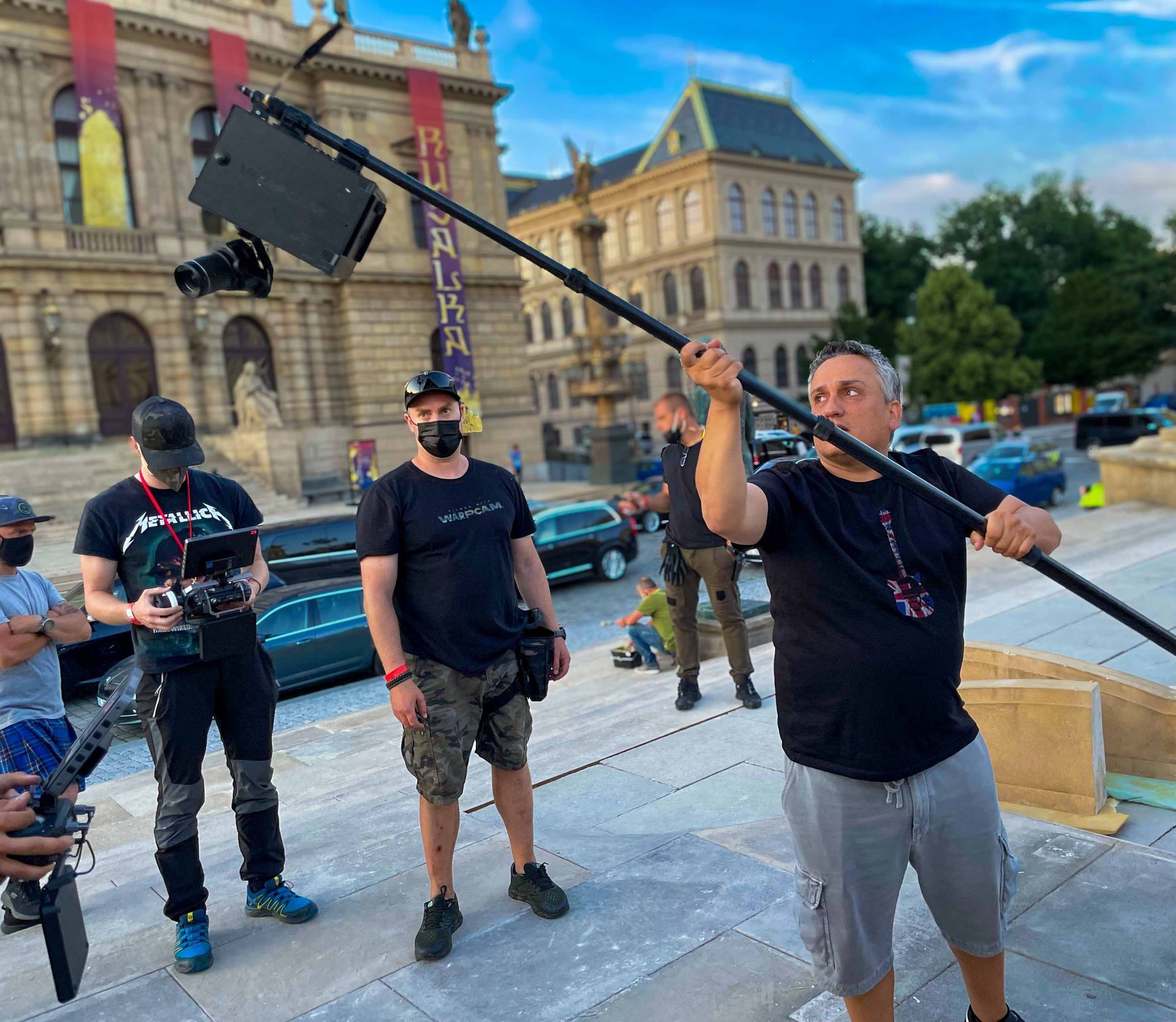Joe Russo holding a pole-mounted WarpCam® prototype on The Gray Man set in Prague with Ferdi Fischer visible in the background.
