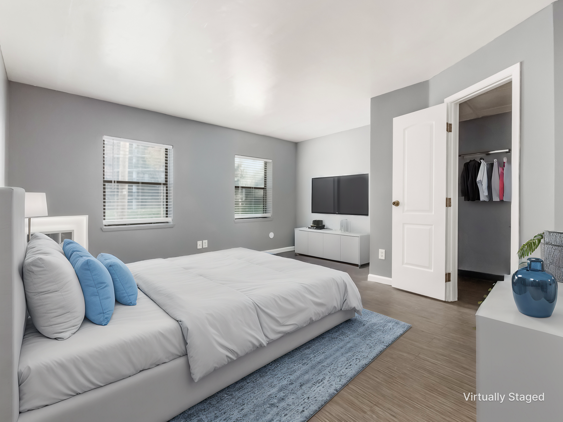 Gray bedroom with white trim, bed, dresser, closet, and blue rug in a bright, minimalist room