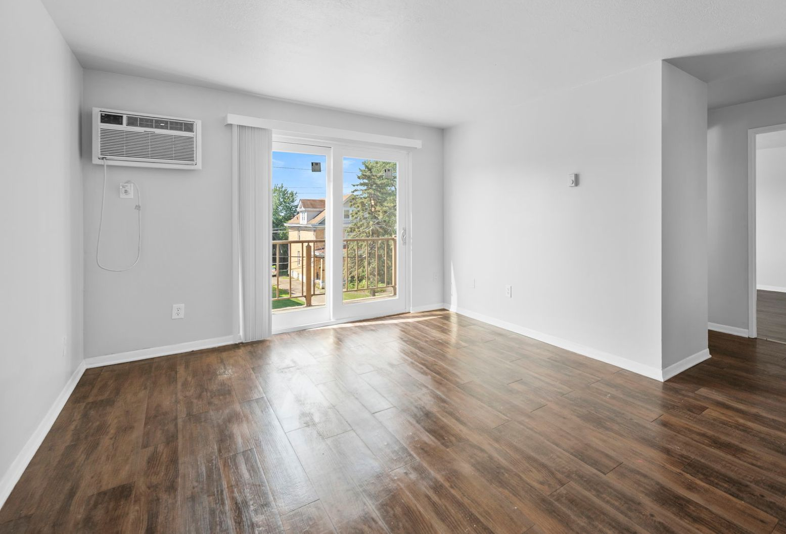 Empty living room with wood floors, white walls, and sliding glass doors to a balcony.