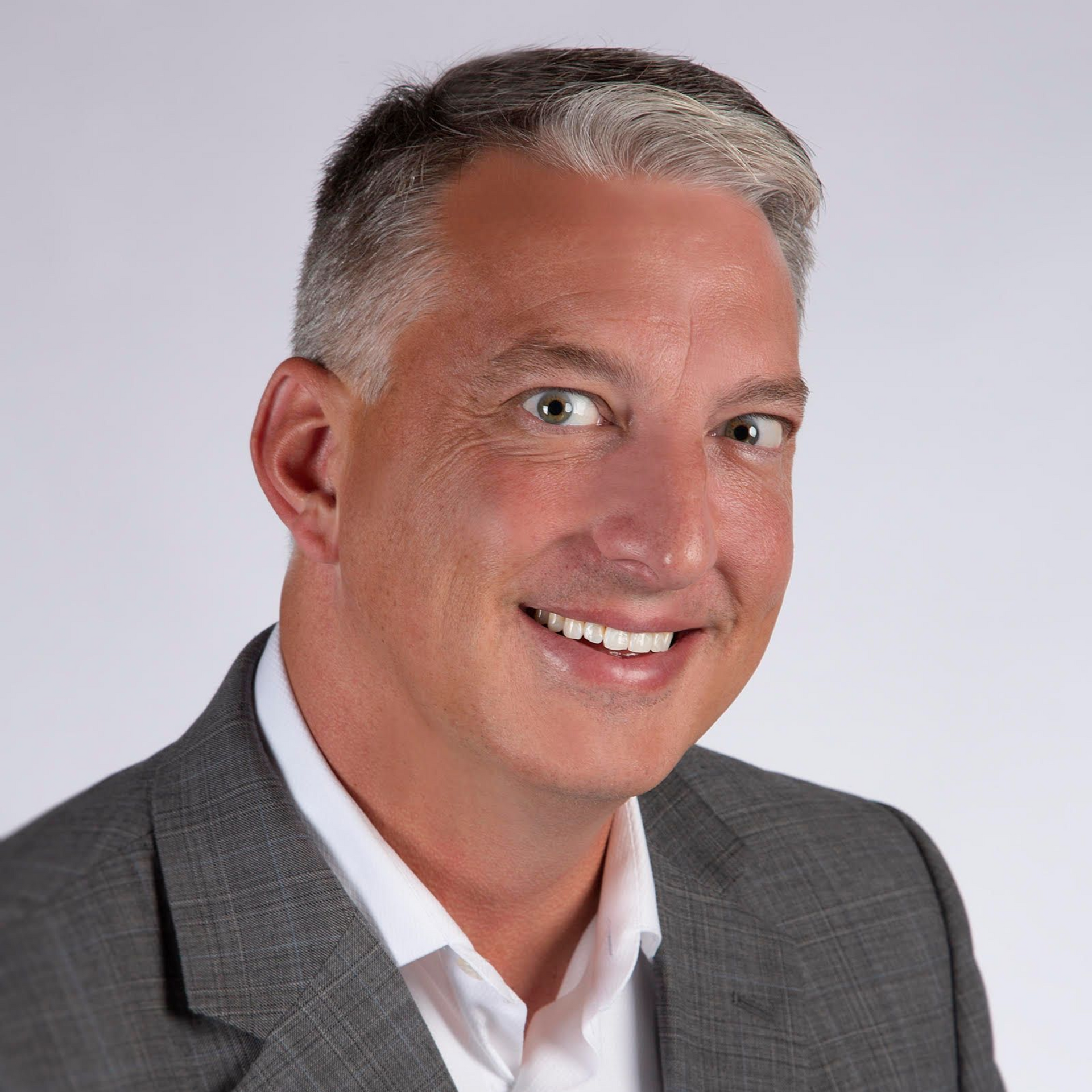 Studio headshot of a smiling man in a gray suit and white shirt on a light background