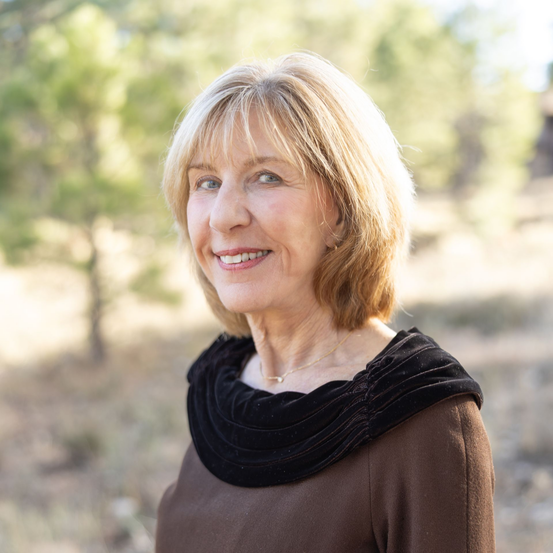 Woman smiling outdoors in a brown sweater with a black cowl neck