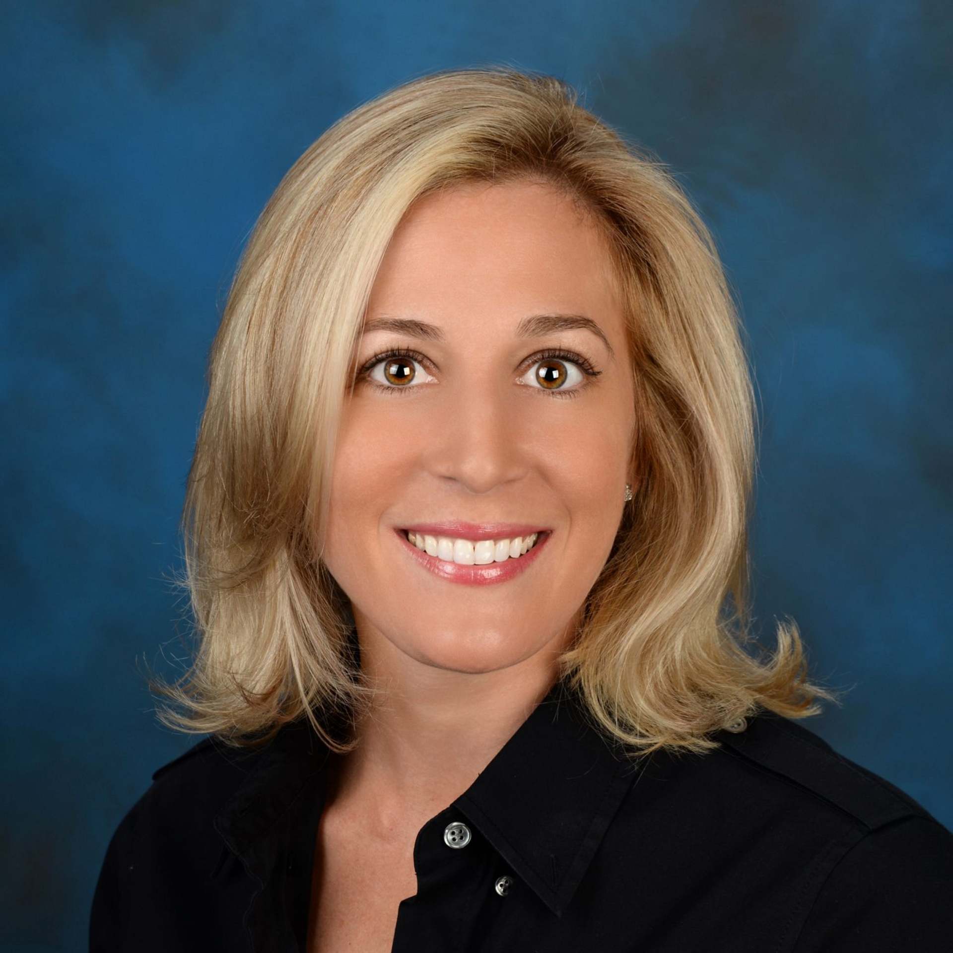 Studio headshot of a smiling woman in a black blouse against a blue background