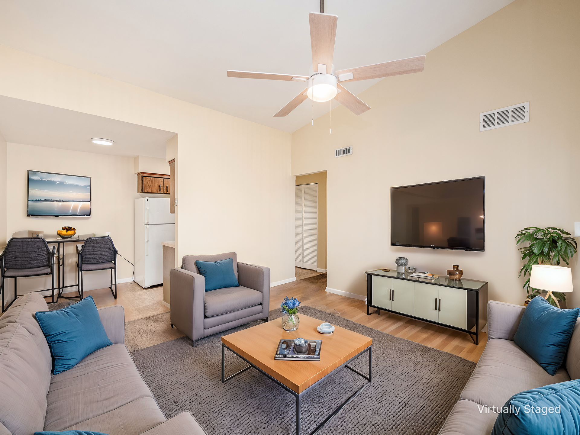 Bright living room with gray sofas, blue cushions, wall-mounted TV, coffee table, and ceiling fan