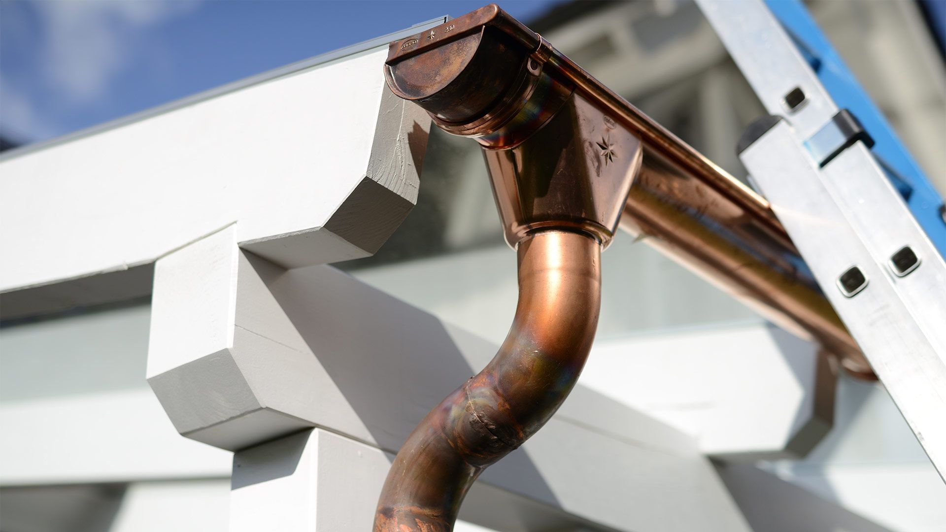 A close up of a copper gutter with a ladder in the background.