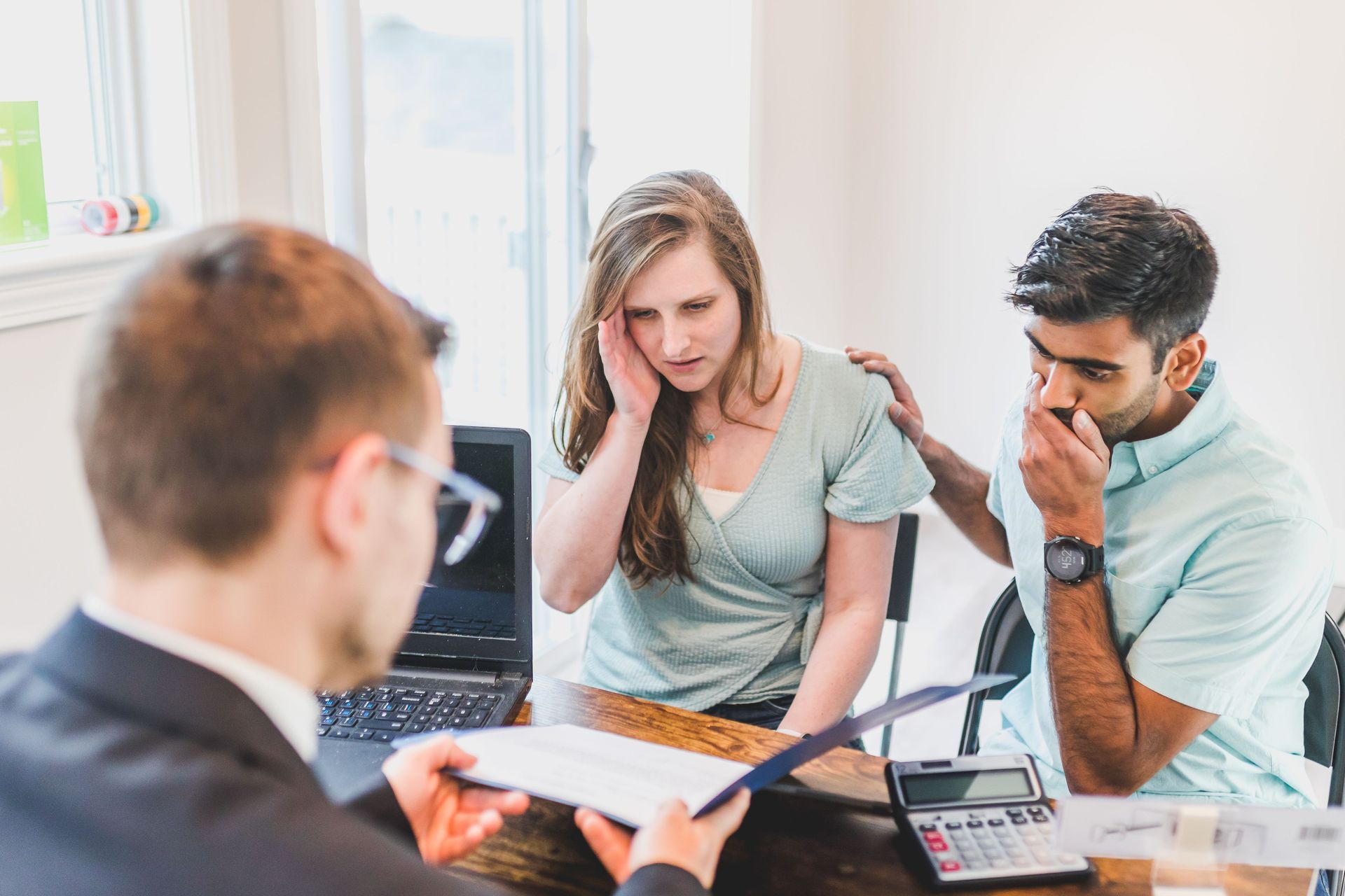 Office meeting with three people reviewing documents, one woman looks stressed while two others listen attentively