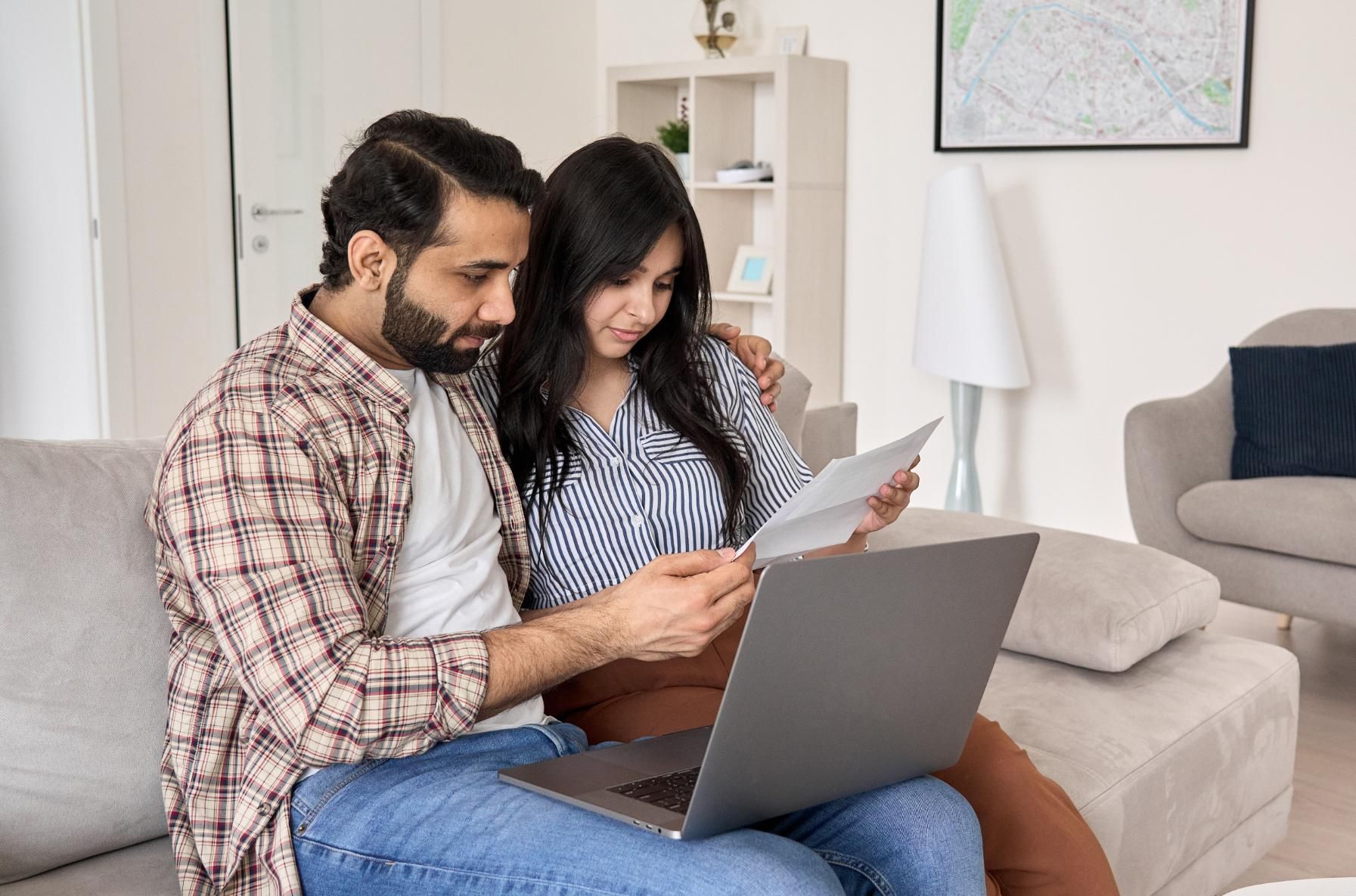 A man and a woman are sitting on a couch looking at a laptop.