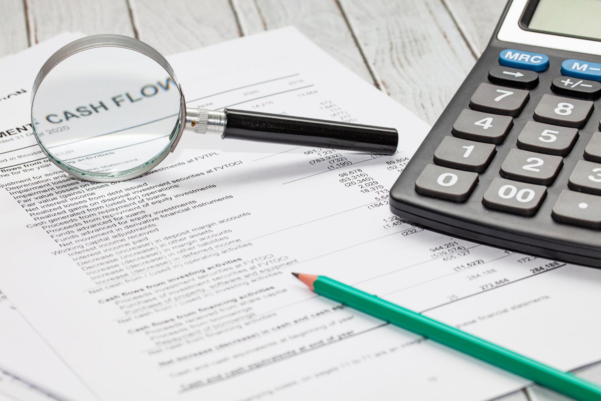 A calculator, magnifying glass, pen ,and pencil are on a table.
