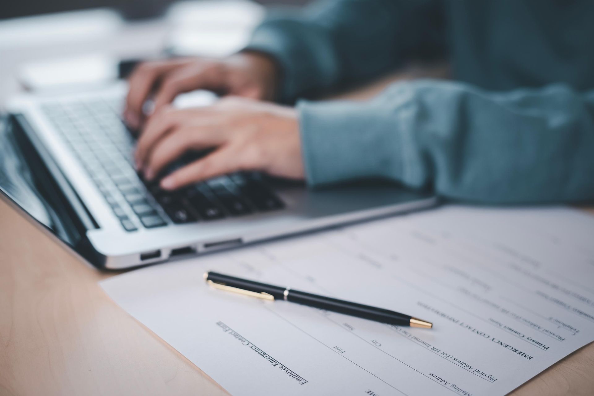 A person is typing on a laptop computer next to a pen.