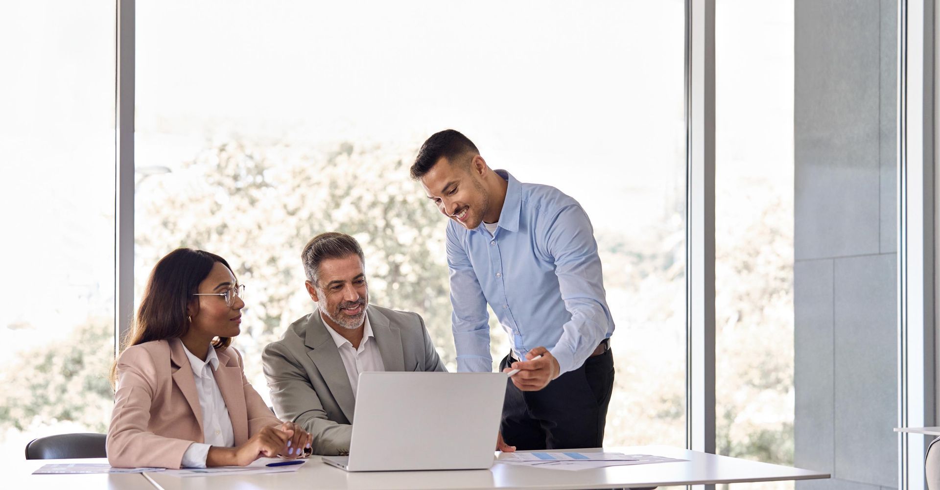 A group of business people are sitting around a table looking at a laptop computer.