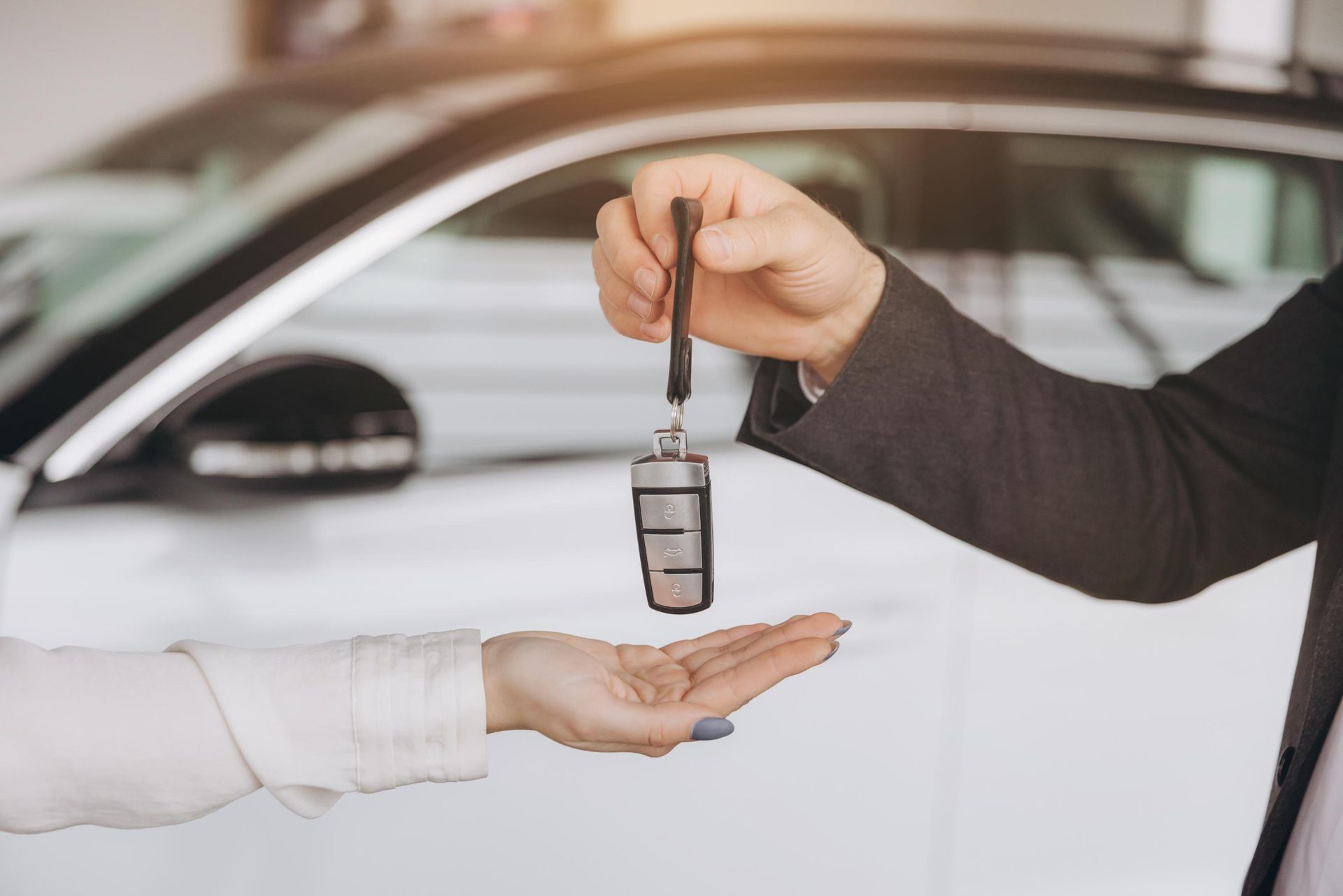 A man is handing a car key to a woman in front of a car.