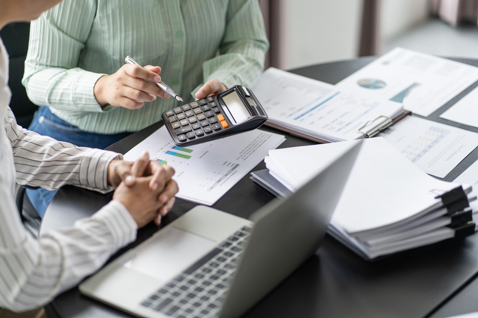 A man and a woman are sitting at a table with a laptop and a calculator.