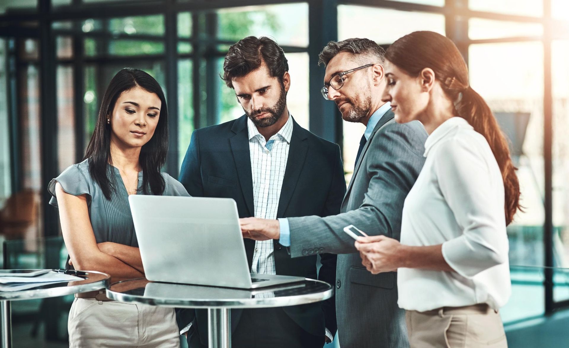 A group of people are standing around a table looking at a laptop computer.