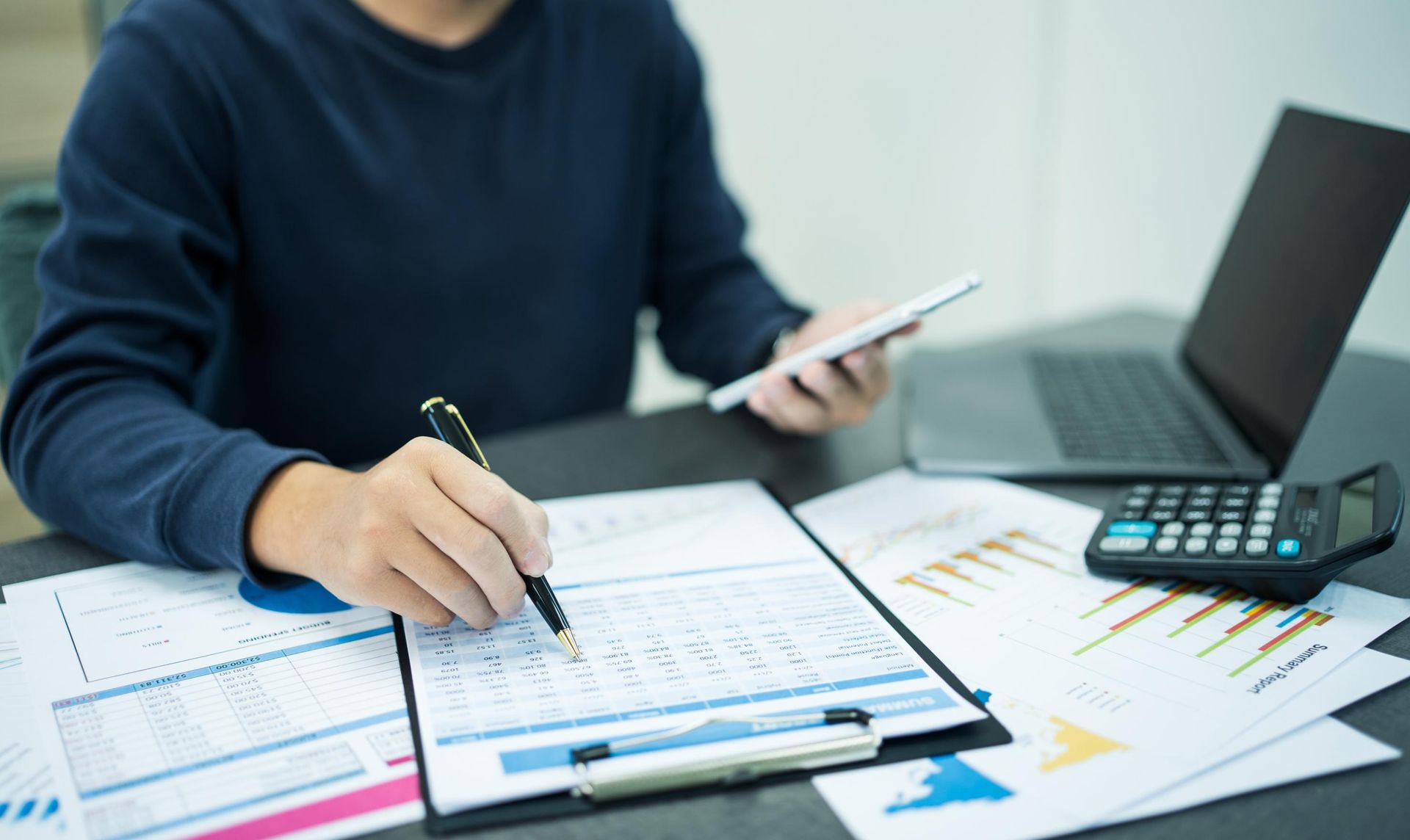 A man is sitting at a table using a tablet and a calculator.
